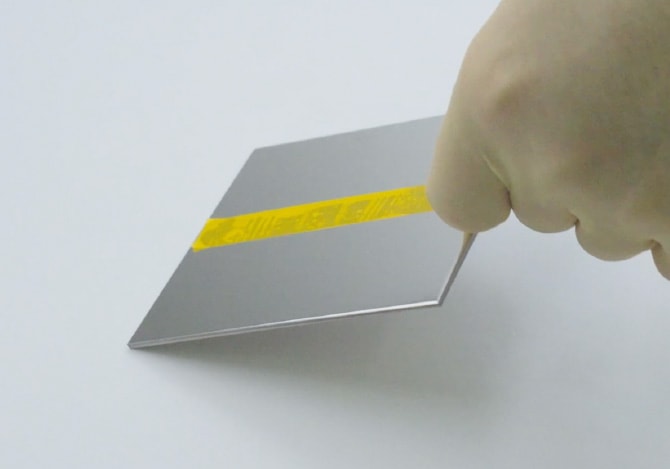 非粘着コーティングされていないステンレス板が、粘着テープの接着力によって持ち上がっている様子